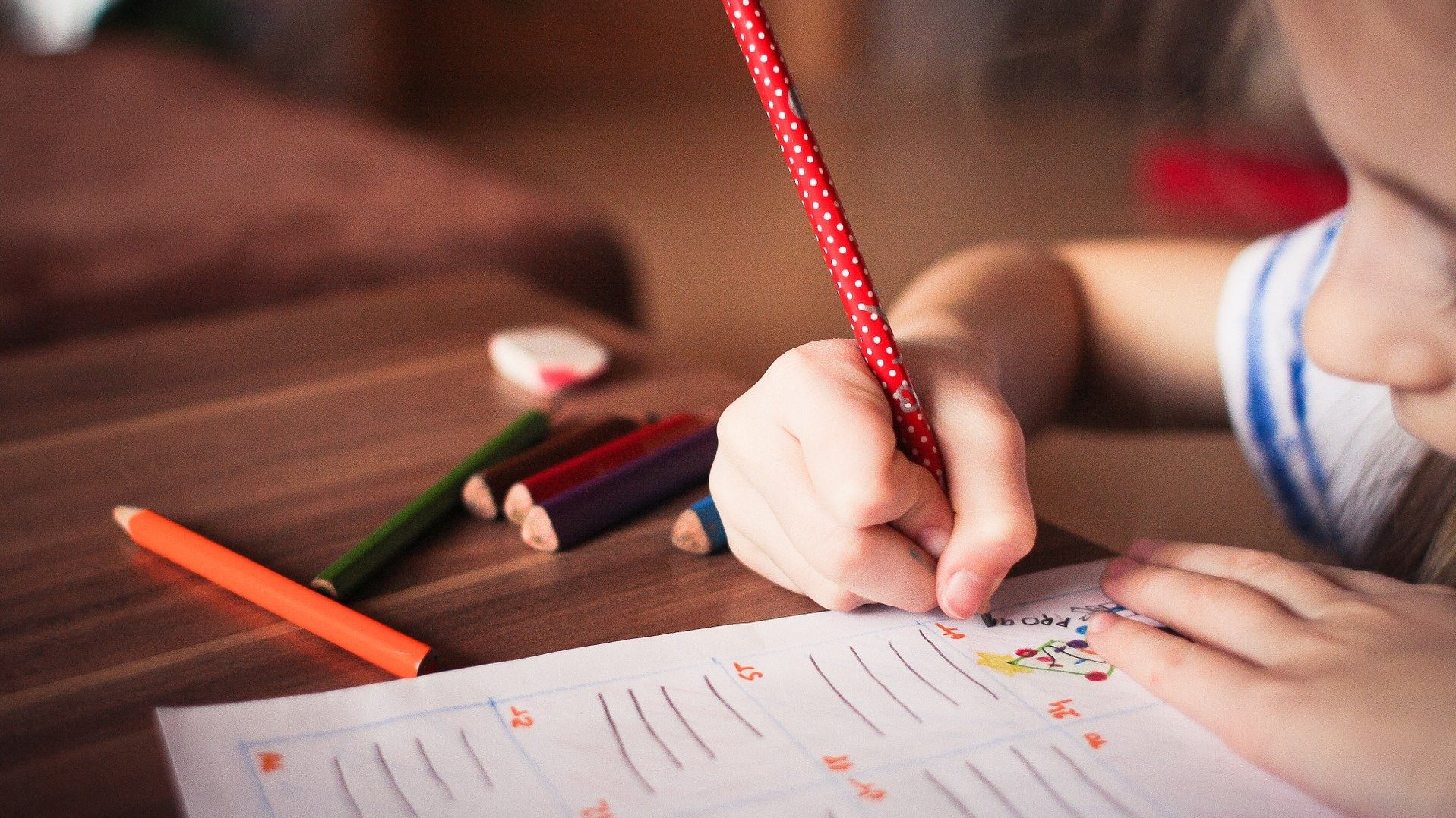 Auf diesem Bild ist ein Kind zu sehen, welches auf einem weißen Papier schreibt und malt.