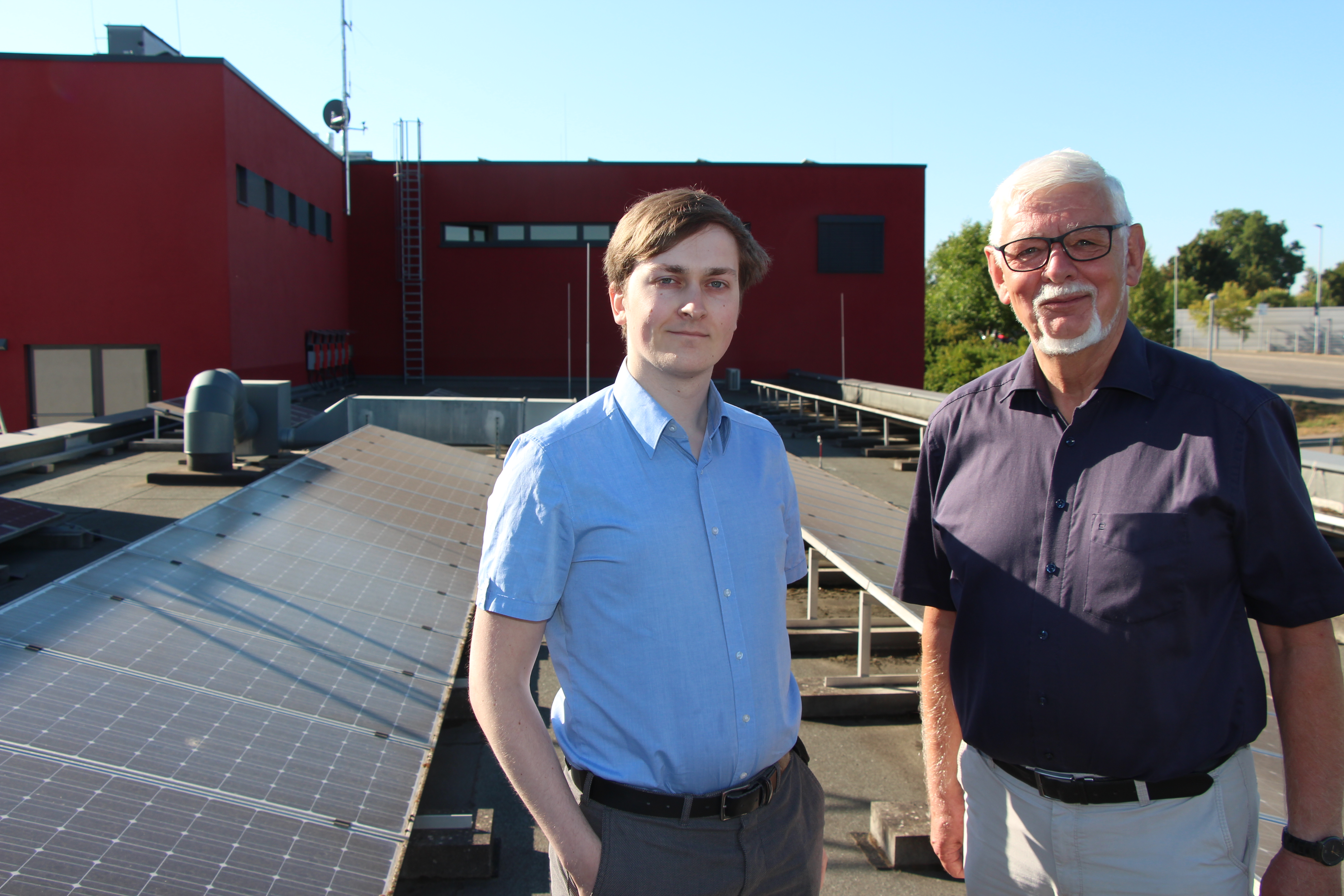 Doktor Helmut Randoll und Thomas Eckstein stehen auf einem Dach, auf dem Solaranlagen verbaut sind